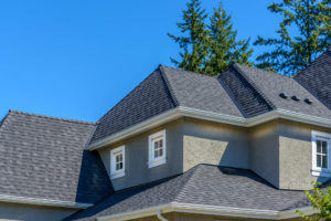 The top of a home in a suburban neighborhood. It has a gray asphalt shingle roof.