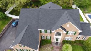 Aerial view of an upscale two-story brick home with multiple roof peaks and a new charcoal-colored roof